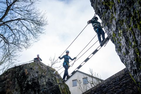 Zwei Kletterer gehen zwischen zwei Felsen über eine Hängebrücke.
