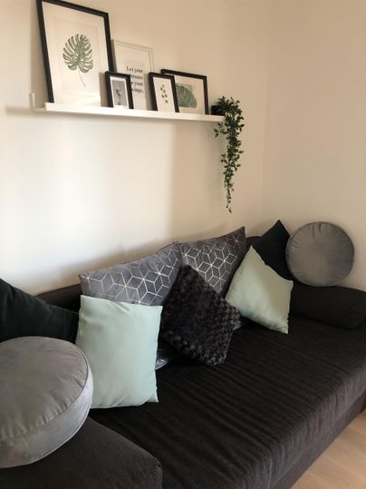 Een elegante bank met verschillende kussens in zachte kleuren. Op de achtergrond hangen er foto's aan de muur en een plant is decoratief geplaatst.