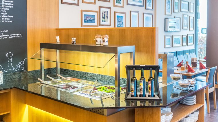 Ein einladender Essbereich mit einem Salatbuffet und Holzregalen. An der Wand hängen verschiedene Bilder, die eine gemütliche Atmosphäre schaffen.