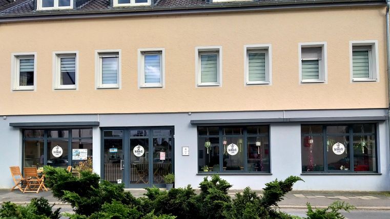 Ein modernes Geschäftshaus mit einer hellen Fassade. Vor dem Gebäude stehen einige Möbel und es gibt große Fenster mit einladenden Schildern.