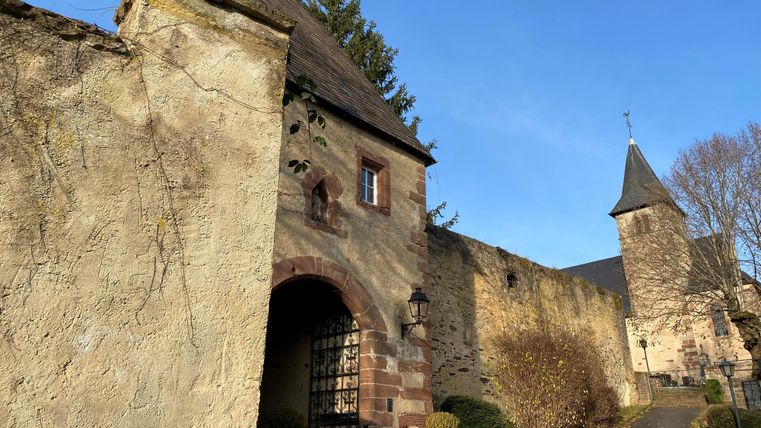 Une porte historique avec un mur en pierre et une tour attenante. Le ciel est clair et bleu.