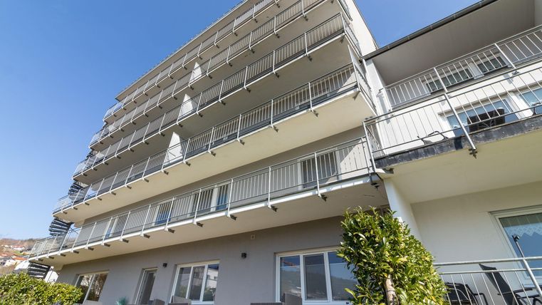 Ein modernes Gebäude mit mehreren Balkonen und einer klaren blauen Himmel. Es gibt liegengebliebene Möbel im Freien und eine grüne Rasenfläche.