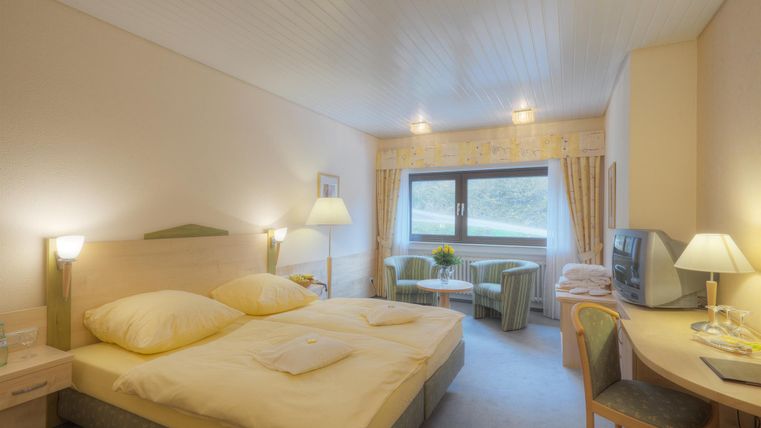 Ein gemütliches Schlafzimmer mit einem Doppelbett und hellen Farben. Es gibt einen Schreibtisch und einen gemütlichen Sitzbereich.