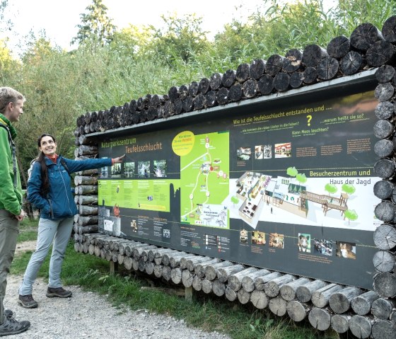 Zwei Personen betrachten eine Informationstafel im Naturparkzentrum Teufelsschlucht. Die Tafel zeigt Karten und Informationen &uuml;ber die Umgebung., &copy; Eifel Tourismus GmbH, Dominik Ketz