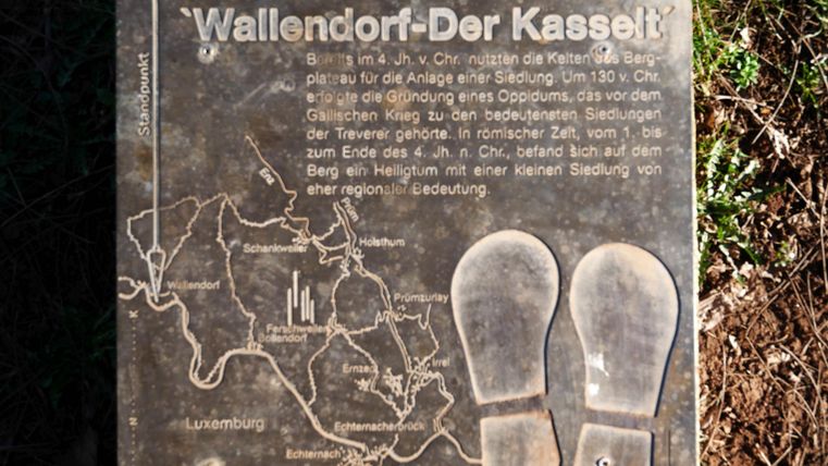 Ein Informationsschild über Wallendorf-Der Kasselt, das eine Karte und Fußabdrücke zeigt. Es beschreibt die historische Bedeutung der Gegend und ihre Siedlungsgeschichte.