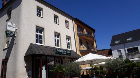 Ein charmantes Gebäude mit mehreren Fenstern und einem Eingang. Vor dem Haus stehen Sonnenschirme und Pflanzen.