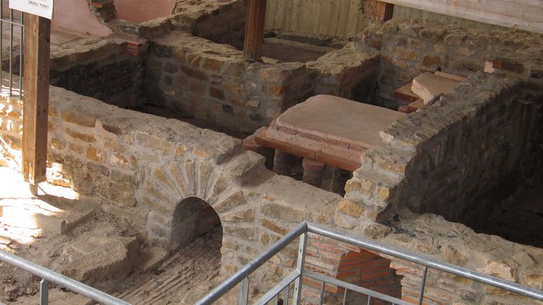 Die Überreste eines alten Gebäudes sind sichtbar. Steinmauern und Strukturen sind gut erhalten und werden von einem Holzrahmen geschützt.