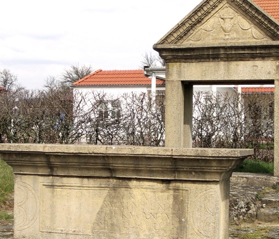 Replica of a Gallo-Roman votive monument with inscription, modern buildings and bare bushes in the background., &copy; Elke Wagner, Felsenland S&uuml;deifel Tourismus GmbH