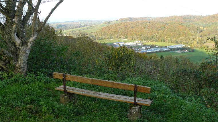 Holzbank mit Blick auf eine Landschaft mit Hügeln und einem Industriegebiet.