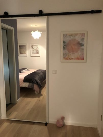 Een moderne kamer met een schuifdeur die naar een slaapkamer leidt. Aan de muur hangen schilderijen en er is een zachte gloed van een plafondlamp.