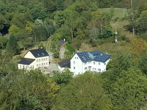 Zwei moderne Häuser in einer grünen Landschaft mit Bäumen. Das größere Haus hat Solarpanele auf dem Dach.