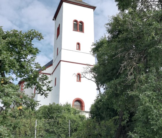 Weiße Kirche mit rotem Dach und Turm, umgeben von grünen Bäumen und blauem Himmel im Hintergrund., © TI Bitburger Land