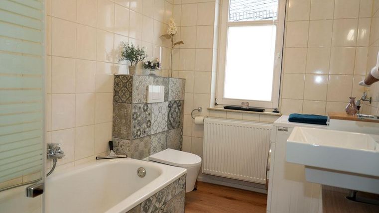 Ein modernes Badezimmer mit einer Badewanne und einem Waschbecken. Die eleganten Fliesen und das Holzdesign schaffen eine ansprechende Atmosphäre. Es steht Ihnen ein Waschtrockner zur Verfügung.