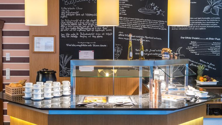 Ein einladender Empfangsbereich mit einem modernen Thekenaufbau. Im Hintergrund sind Informationen an einer Tafel geschrieben und Geschirr zum Servieren bereitgestellt.