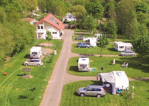 Ein gepflegter Campingplatz mit mehreren Wohnmobilen und Fahrzeugen. Umgeben von grüner Landschaft und Bäumen.