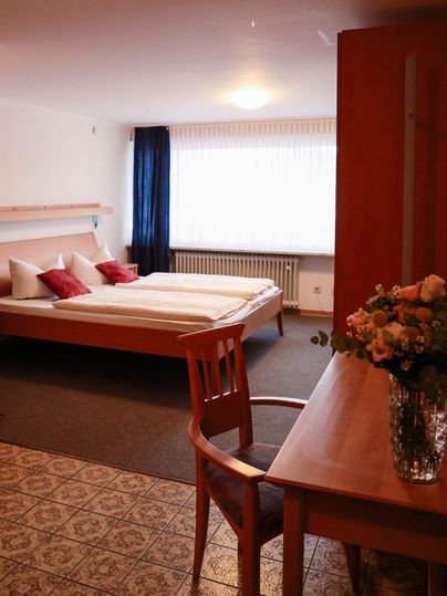 Ein gemütliches Schlafzimmer mit einem großen Bett und roten Kissen. Ein Tisch mit einer Vase voller Blumen ist neben dem Bett platziert.