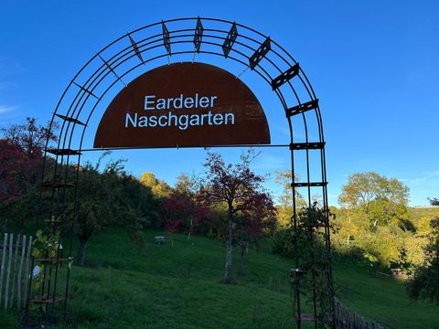 Ein Eingangsbereich mit einem Bogen aus Metall, auf dem "Eardeler Naschgarten" steht. Im Hintergrund sieht man eine grüne Wiese mit Bäumen.
