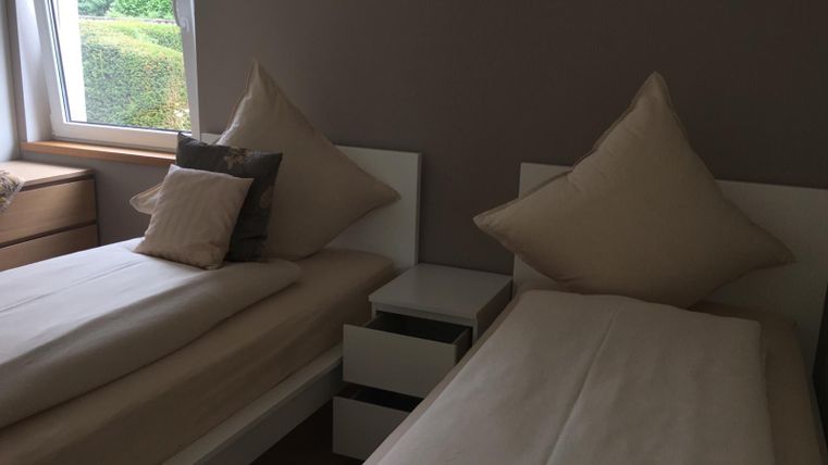 Ein gemütliches Schlafzimmer mit zwei Einzelbetten und großen Kissen. Der Raum hat ein Fenster, das Tageslicht hereinlässt.