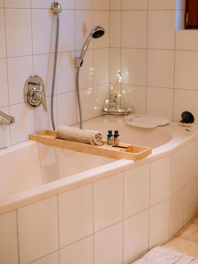Een moderne badkamer met een bad en houten elementen. Op de badrand liggen een handdoek en enkele etherische oliën.