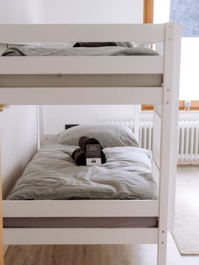 Een eenvoudige slaapkamer met een stapelbed. De bedden zijn versierd met grijze beddengoed en een kussen.