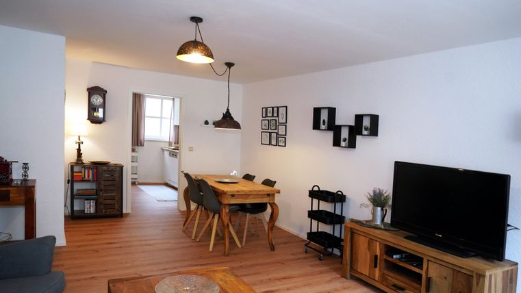Ein gemütliches Wohnzimmer mit einem Essbereich und einem großen Fernseher. Die hellen Wände und der Holzboden sorgen für eine einladende Atmosphäre.