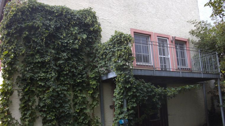 Ein charmantes Haus mit einem Balkon und viel grünem Efeu. Die Fassade wirkt freundlich und einladend.