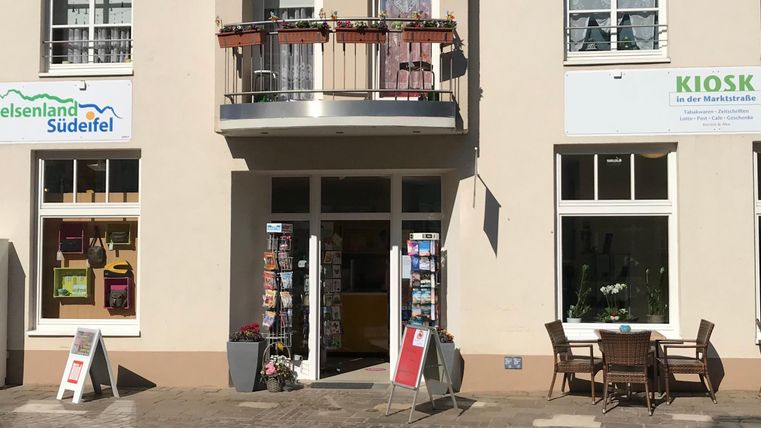 Ein freundliches Geschäft mit einem Kiosk und einem Informationszentrum. Draußen stehen Tische und Stühle für Gäste.