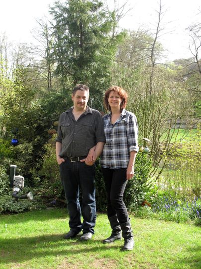 Ein Paar steht lächelnd im Garten. Um sie herum sind Bäume und frisches, grünes Gras.