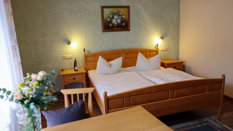 Ein gemütliches Schlafzimmer mit einem Doppelbett und Holzmöbeln. Eine Blumen vase und ein Tisch vervollständigen die angenehme Atmosphäre.