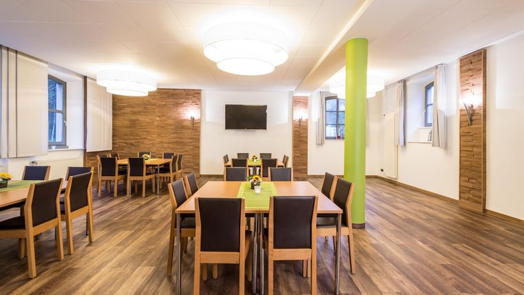 Ein moderner Besprechungsraum mit Holzfußboden und großen Fenstern. Die Tische sind ordentlich angeordnet und mit grünen Tischdecken dekoriert.