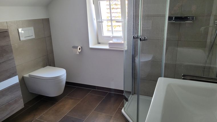 Ein modernes Badezimmer mit einer Dusche und einer Badewanne. Die Wände sind in hellen Farbtönen gehalten und es gibt ein Fenster, das viel natürliches Licht hereinlässt.