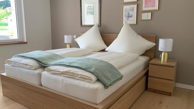 Ein modernes Schlafzimmer mit einem Doppelbett und großen, gemütlichen Kissen. An der Wand hängen gerahmte Bilder und die Fenster bieten einen Blick nach draußen.