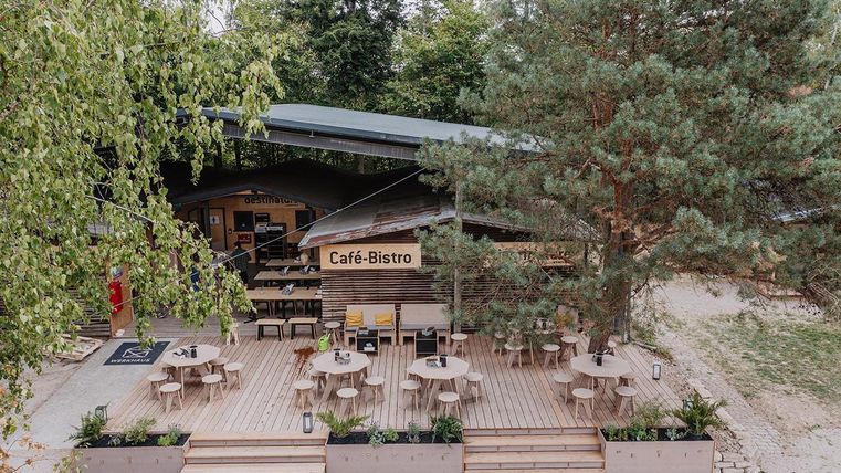 Ein gemütliches Café-Bistro mit einer Terrasse aus Holz. Umgeben von Bäumen, lädt es zum Verweilen und Entspannen ein.