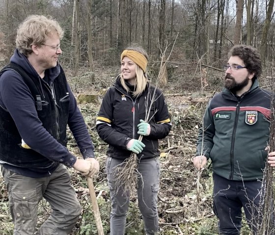 Unter der Leitung von Förster Julian Gröber haben viele Freiwillige bei der Baumpflanzaktion in Ernzen geholfen. (v. l. n. r.: Bruno Zwank und Anna Carina Krebs (Geschäftsführer und Tourismusmanagerin der Felsenland Südeifel Tourismus GmbH), Julian Gröber (Revierförster)., © Felsenland Südeifel Tourismus GmbH