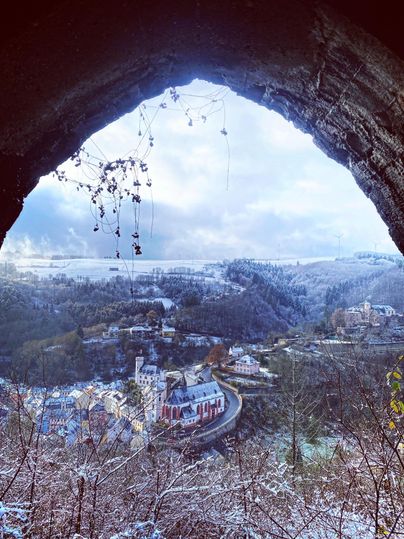 Eine malerische Winterlandschaft mit schneebedeckten Bäumen und einem Blick auf ein kleines Dorf. Der Himmel ist teilweise bewölkt, und die Szenerie strahlt Ruhe aus.