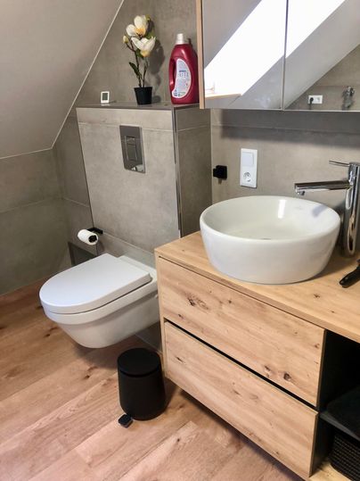 Ein modernes Badezimmer mit einem eleganten Waschbecken und einer Toilette. Holz- und graue Elemente verleihen dem Raum ein zeitgemäßes Design.