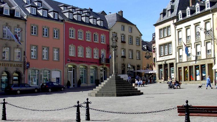 Ein schöner Platz mit bunten Gebäuden und einer Statue in der Mitte. Es gibt einige Menschen, die sich dort aufhalten und das Wetter genießen.