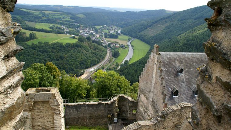 Ein Blick von einer alten Burgruine auf eine grüne Landschaft. Im Hintergrund fließt ein Fluss und verläuft entlang des Hügels.