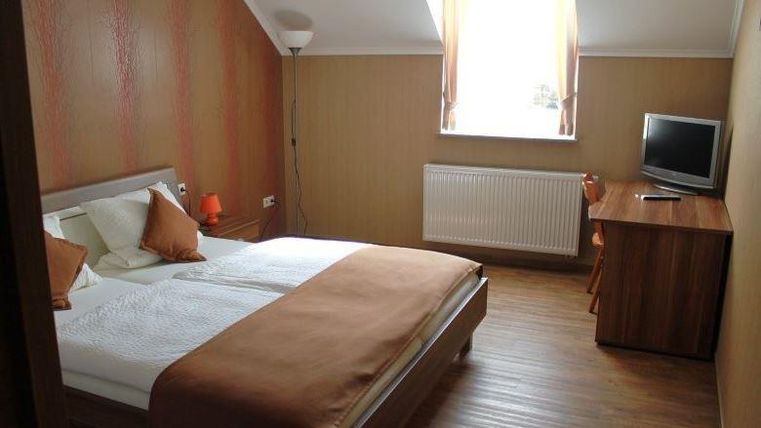 Une chambre lumineuse et moderne avec un lit double et des coussins confortables. Il y a un bureau, une télévision et une grande fenêtre pour beaucoup de lumière naturelle.