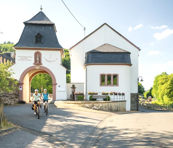 Cyclists on the Kyll cycle path in front of the gate of St. Thomas Monastery, © Eifel Tourismus GmbH