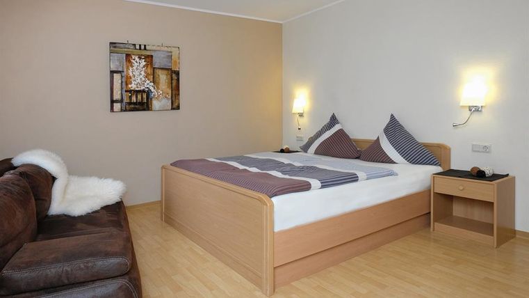 Ein gemütliches Zimmer mit einem Doppelbett und modernen Kissen. Eine Couch und ein Nachttisch ergänzen die entspannte Atmosphäre.