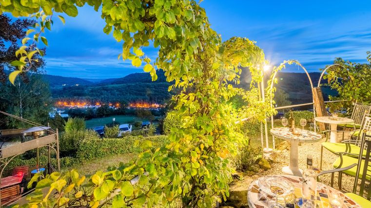 Ein schöner Ausblick auf die Rosenterrasse mit Weinreben und einem stimmungsvollen Abendlicht. Tische sind für Gäste im Freien vorbereitet.