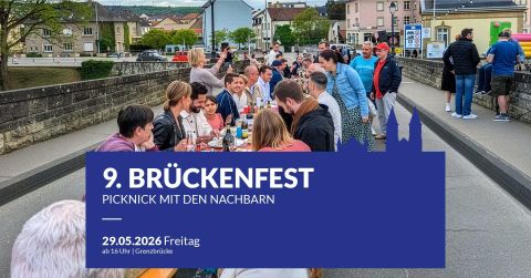 Eine belebte Brücke mit vielen Menschen, die über einen Fluss führt. Im Hintergrund sind malerische Häuser und etwas Grün sichtbar.