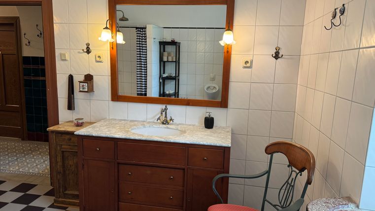 Une salle de bain élégante avec un grand miroir et un meuble lavabo moderne. Les murs sont carrelés de manière claire, et le sol a un motif classique en damier.