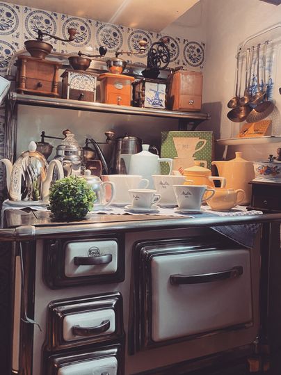 Eine nostalgische Küche mit einem klassischen Herd und feinem Geschirr. Über der Arbeitsfläche hängen verschiedene Küchengeräte und Dekoration.