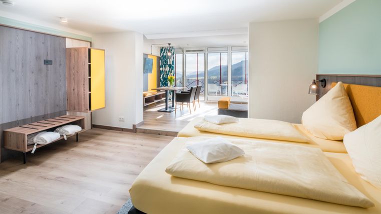 Ein modernes Hotelzimmer mit zwei Betten und hellem Holzfußboden. Große Fenster sorgen für viel Tageslicht und einen Blick nach draußen.