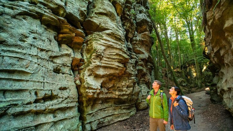 Zwei Wanderer betrachten beeindruckende Felsformationen in einem Waldgebiet.