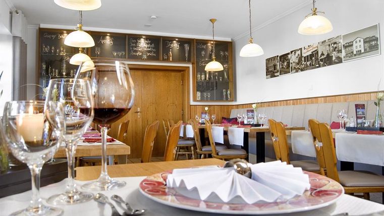 Ein gemütliches Restaurant mit eleganten Tischdecken und festlich gedeckten Tischen. Im Hintergrund sind Bilder an der Wand und warmes Licht von Lampen zu sehen.