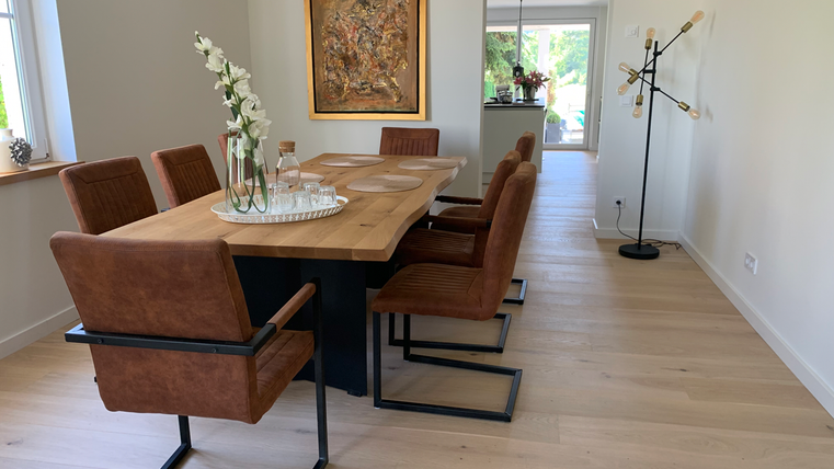 Ein moderner Essbereich mit einem großen Holzwerktisch und stilvollen Stühlen. In der Ecke befindet sich eine dekorative Stehlampe und ein großes Fenster, das viel Licht hereinlässt.