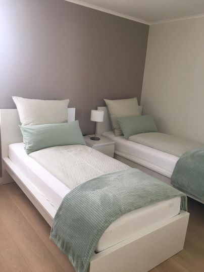 Ein gemütliches Schlafzimmer mit zwei Einzelbetten. Die Wände sind in sanften Farbtönen gehalten, und es gibt eine kleine Nachttischlampe.